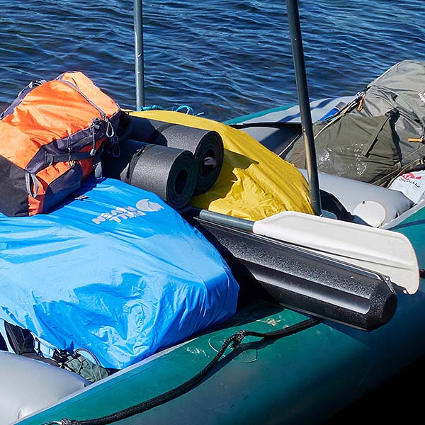 Kajak vollgepackt mit Rucksäcken, Isomatten und Paddel auf einem See.