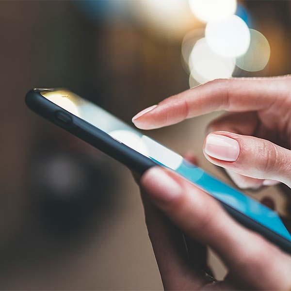 Eine Hand tippt auf das Display eines Smartphones mit unscharfem Hintergrund und Lichteffekten.