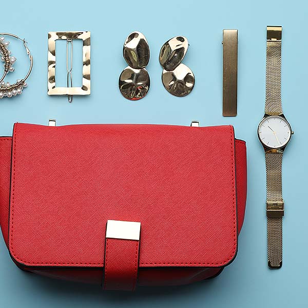 Rote Tasche, goldene Ohrringe, Armbanduhr und Haarschmuck auf blauem Hintergrund.
